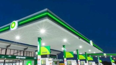 A BP petrol station at night, glowing in green and white, with an attendant present to serve customers.
