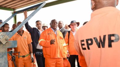 A team of men in orange shirts collaborates around a machine, associated with the Department of Community Safety and Transport.