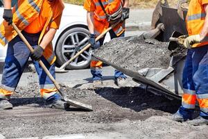 A team of road workers actively repairing a road, dressed in safety attire and utilizing various construction equipment.