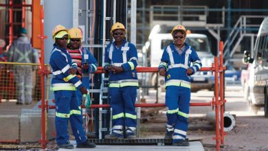 Four men wearing blue and yellow work attire stand on a construction site, highlighting an exciting general worker opportunity.