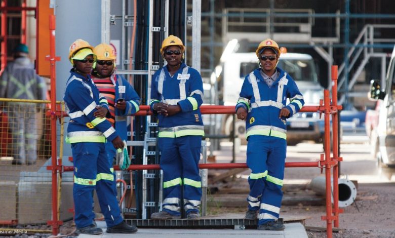 Four men wearing blue and yellow work attire stand on a construction site, highlighting an exciting general worker opportunity.