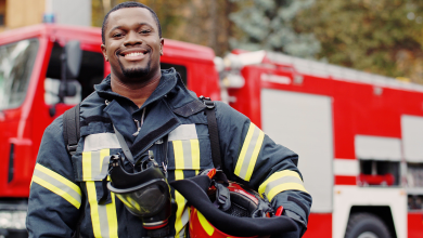 A smiling black man in a firefighter uniform holds a fire hose, promoting the message to become a learner firefighter.